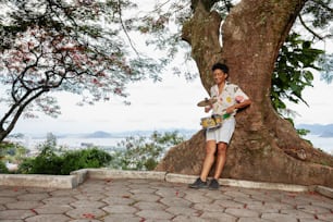 a man standing next to a tree holding a skateboard