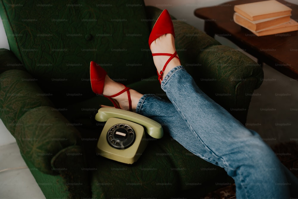 as pernas de uma mulher apoiadas em uma cadeira verde enquanto seguram um telefone