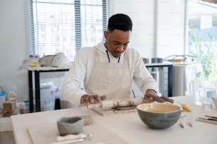 a man in an apron is rolling dough into a bowl