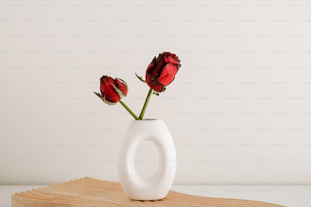a white vase with three red roses in it