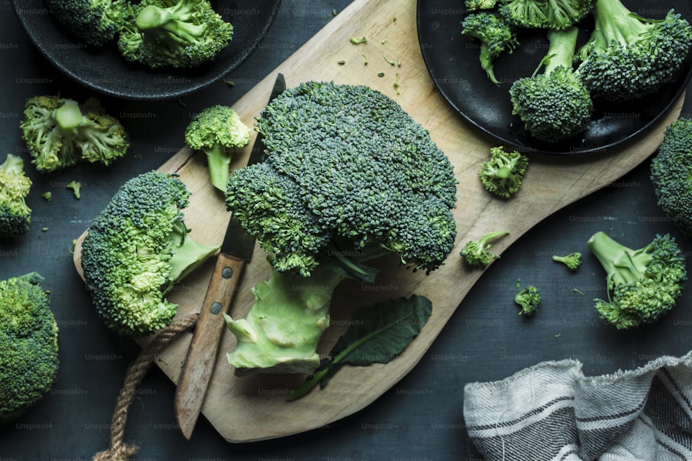 a wooden cutting board topped with broccoli on top of a table