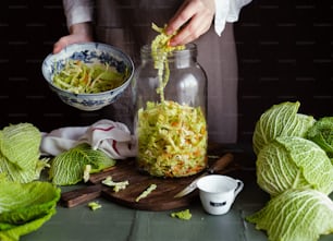 a person in an apron is putting cabbage into a jar