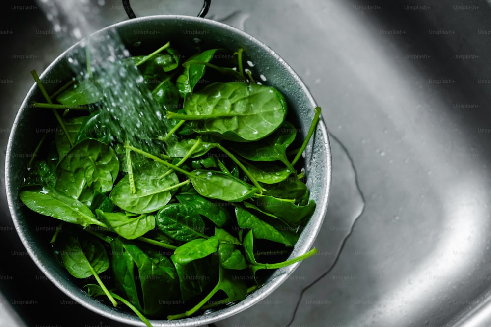 a metal bowl filled with spinach and water