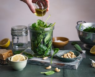 a person pouring olive dressing into a jar of spinach