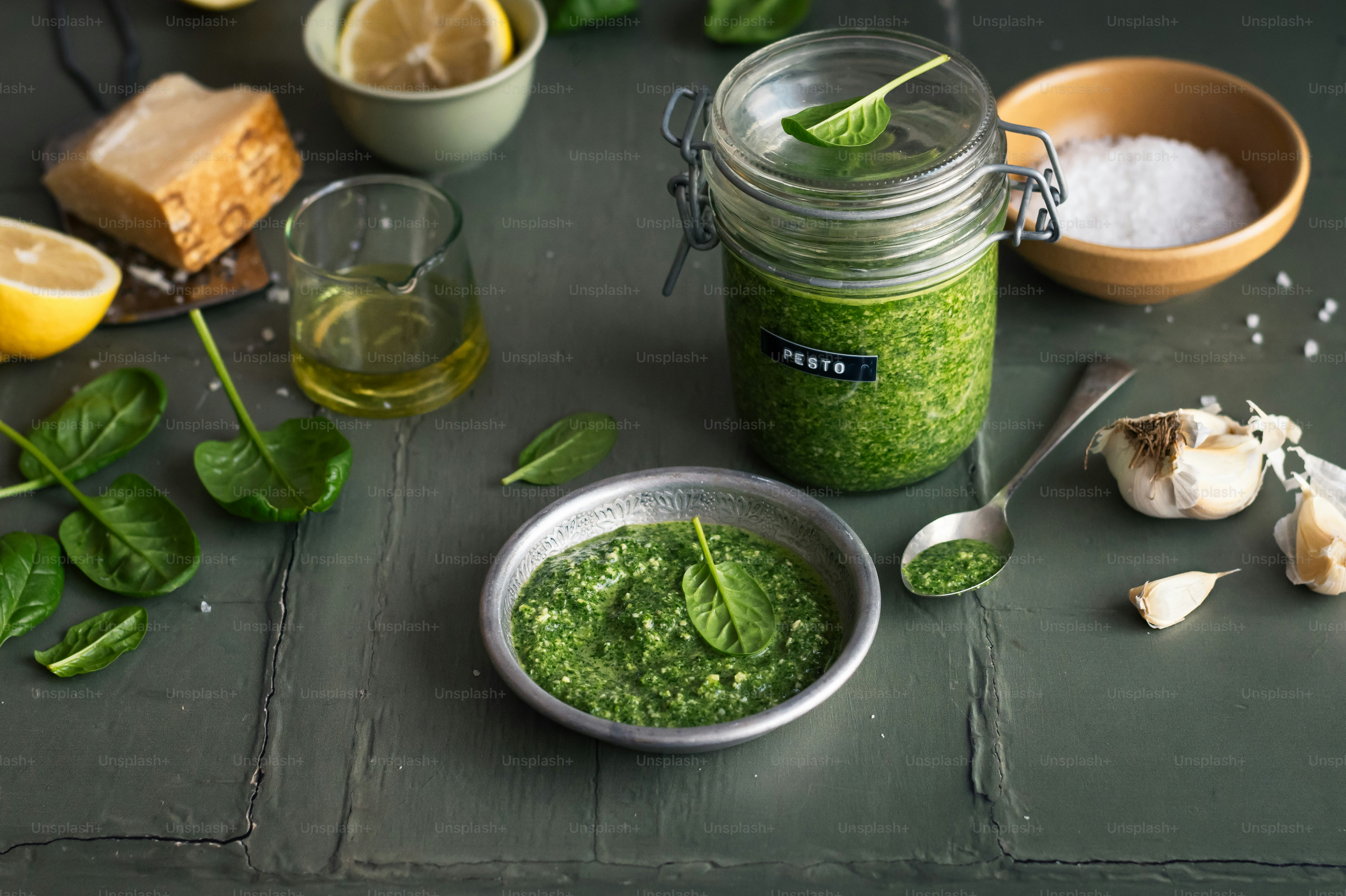 a jar of pesto next to a bowl of garlic and lemon slices