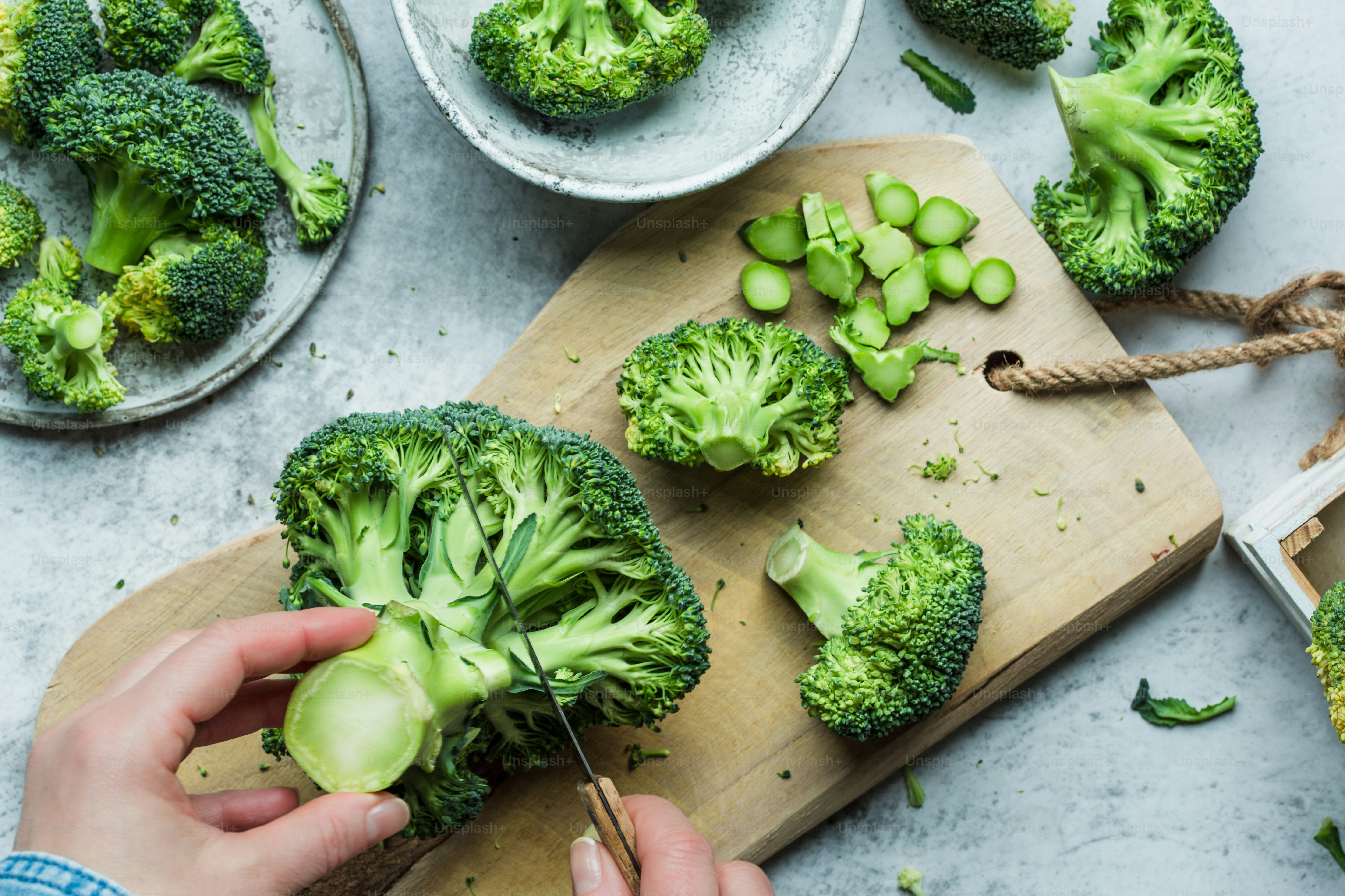 a person cutting broccoli on a cutting board