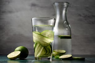 a glass of water with cucumber slices and a pitcher of water