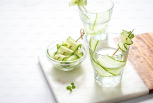 a cutting board topped with glasses filled with cucumbers