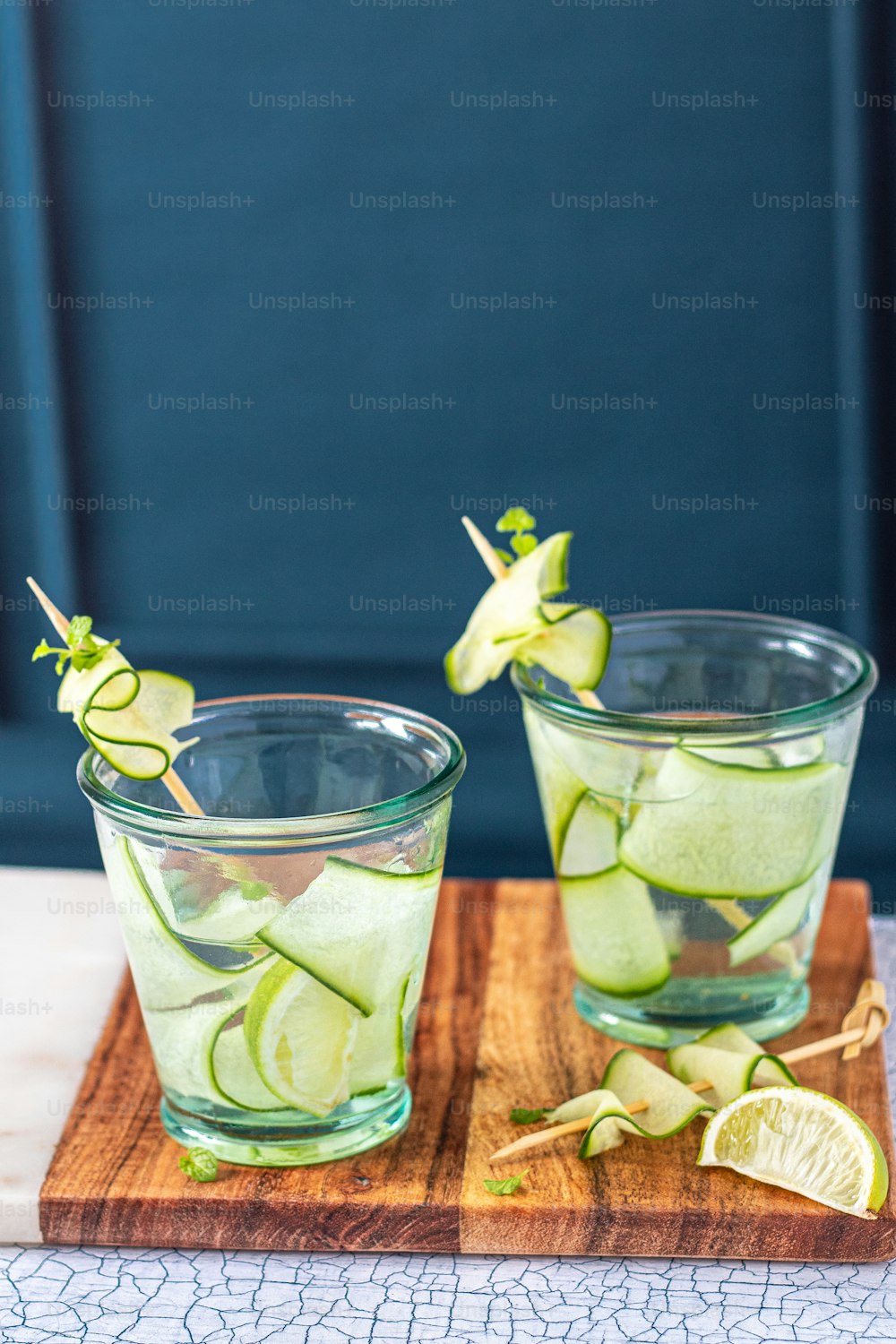two glasses filled with cucumber and lemon on a cutting board