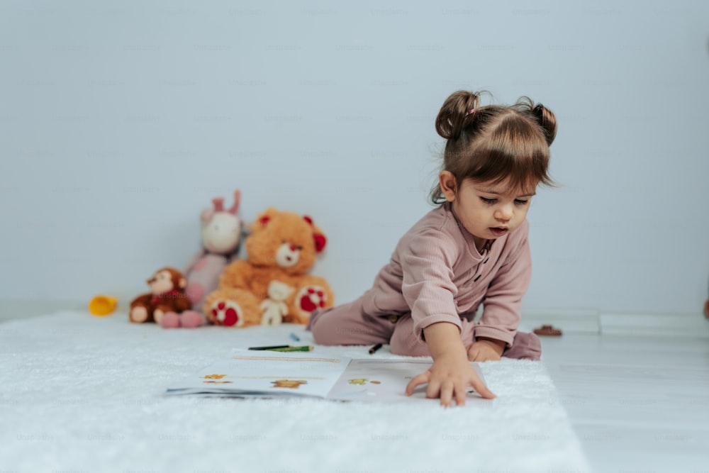 ein kleines Mädchen, das neben einem Teddybären auf dem Boden liegt