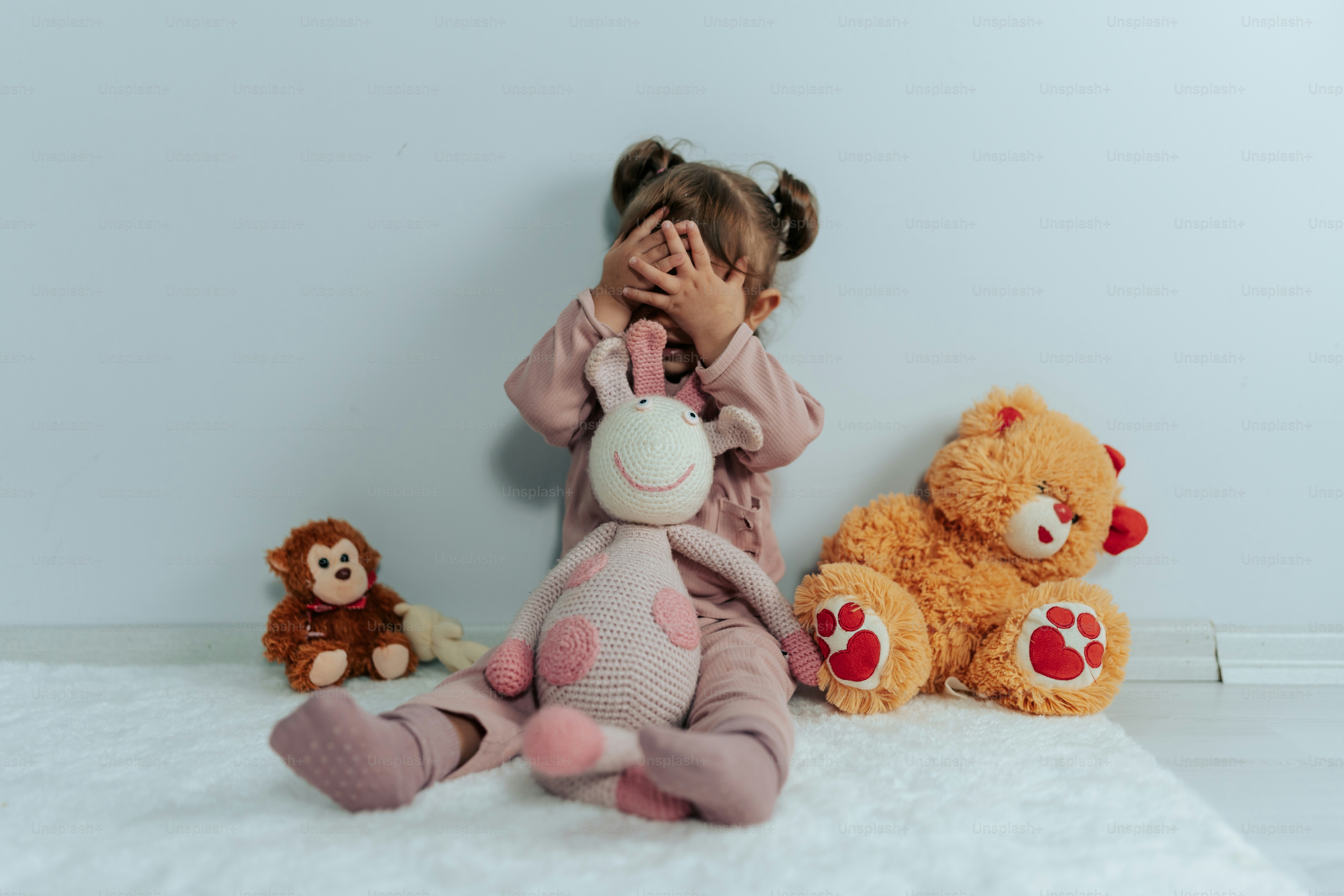 a little girl covering her face next to stuffed animals