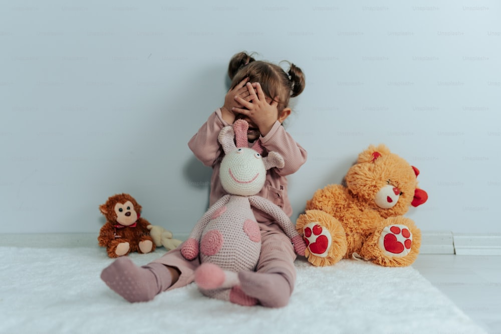 a little girl covering her face next to stuffed animals