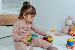 a little girl sitting on the floor playing with a toy