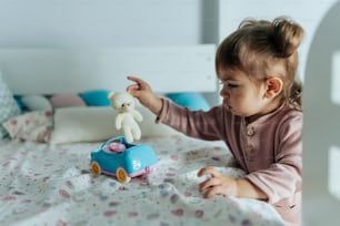 a little girl playing with a teddy bear on a bed