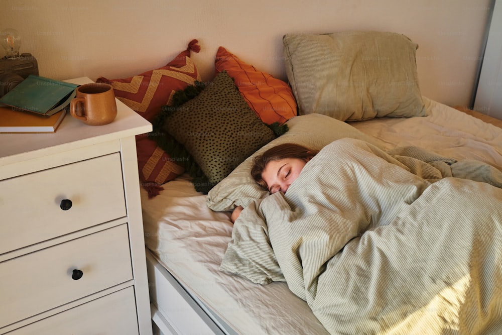 a girl is sleeping in a bed with a blanket