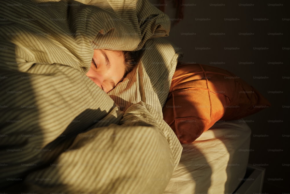 毛布にくるまれてベッドで眠る女性