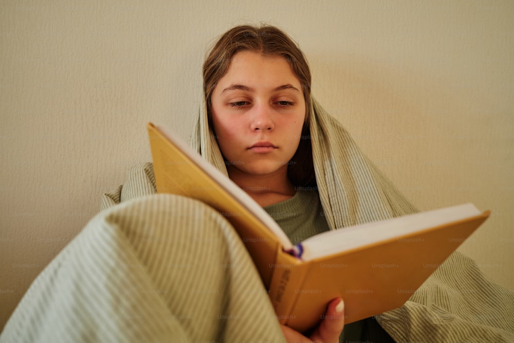 a woman is reading a book under a blanket