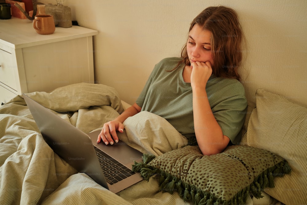eine Frau, die auf einem Bett sitzt und einen Laptop benutzt