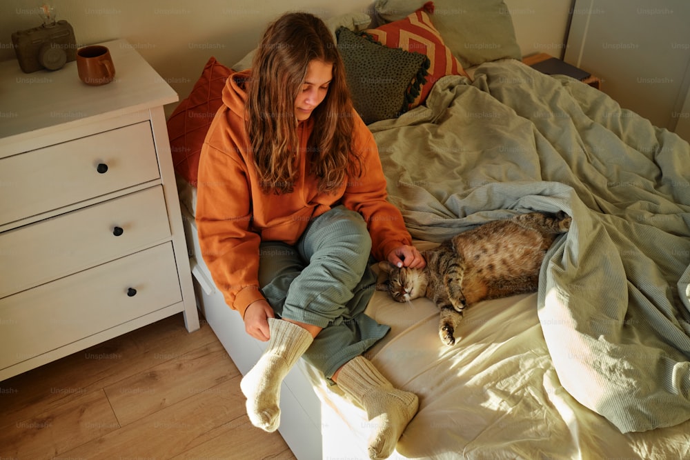 a woman sitting on a bed petting a cat