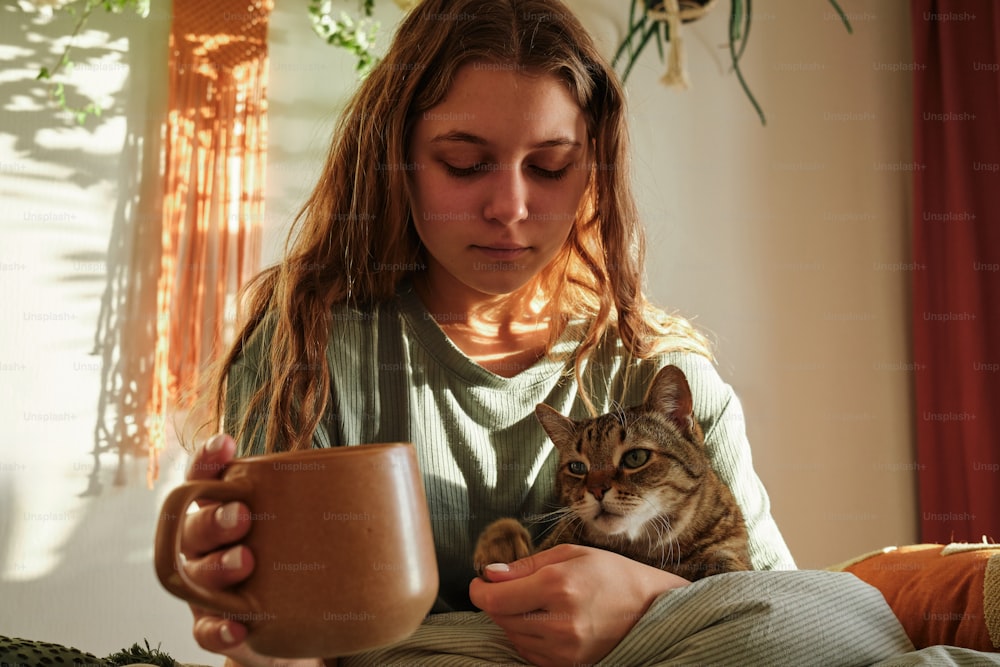 a woman holding a cup of coffee and a cat
