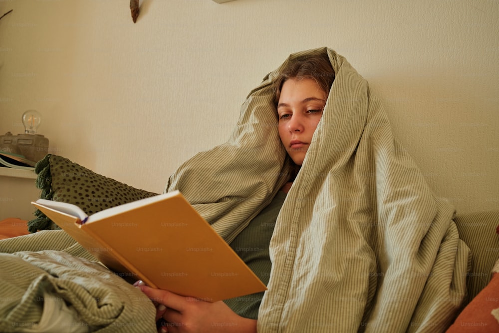 a woman laying in bed under a blanket reading a book