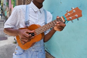 a man holding a ukulele by a blue wall