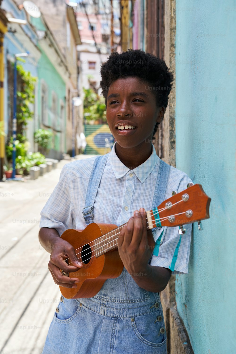 a young man holding a ukulele standing next to a wall