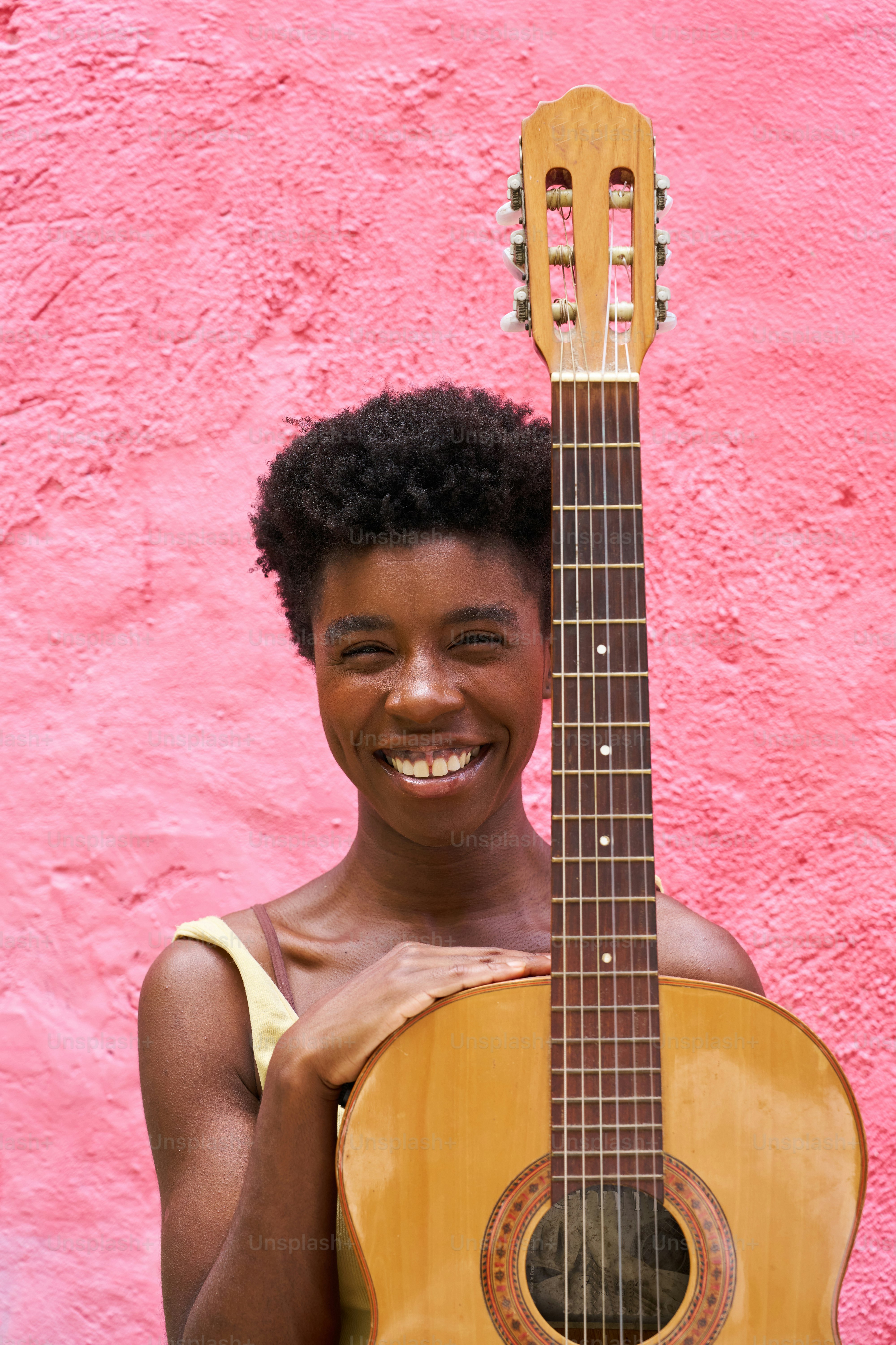 a woman holding a guitar in front of a pink wall