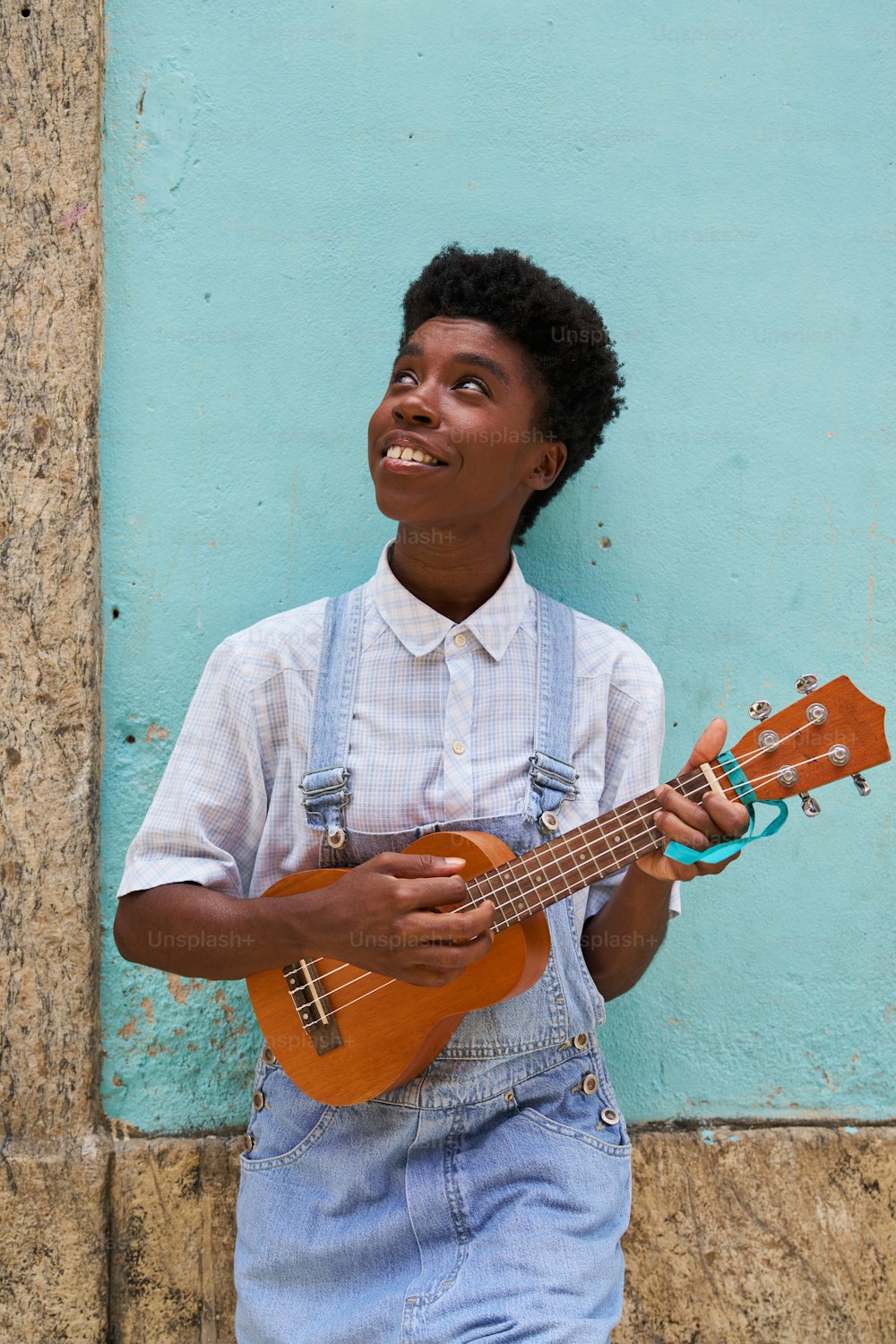 a young man holding a ukulele in front of a blue wall