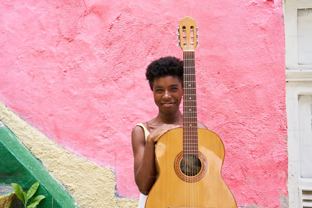 a young man holding a guitar in front of a pink wall