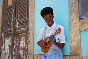 a young man holding a guitar in front of a blue building