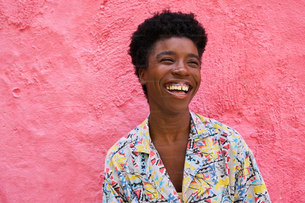 une femme souriant devant un mur rose