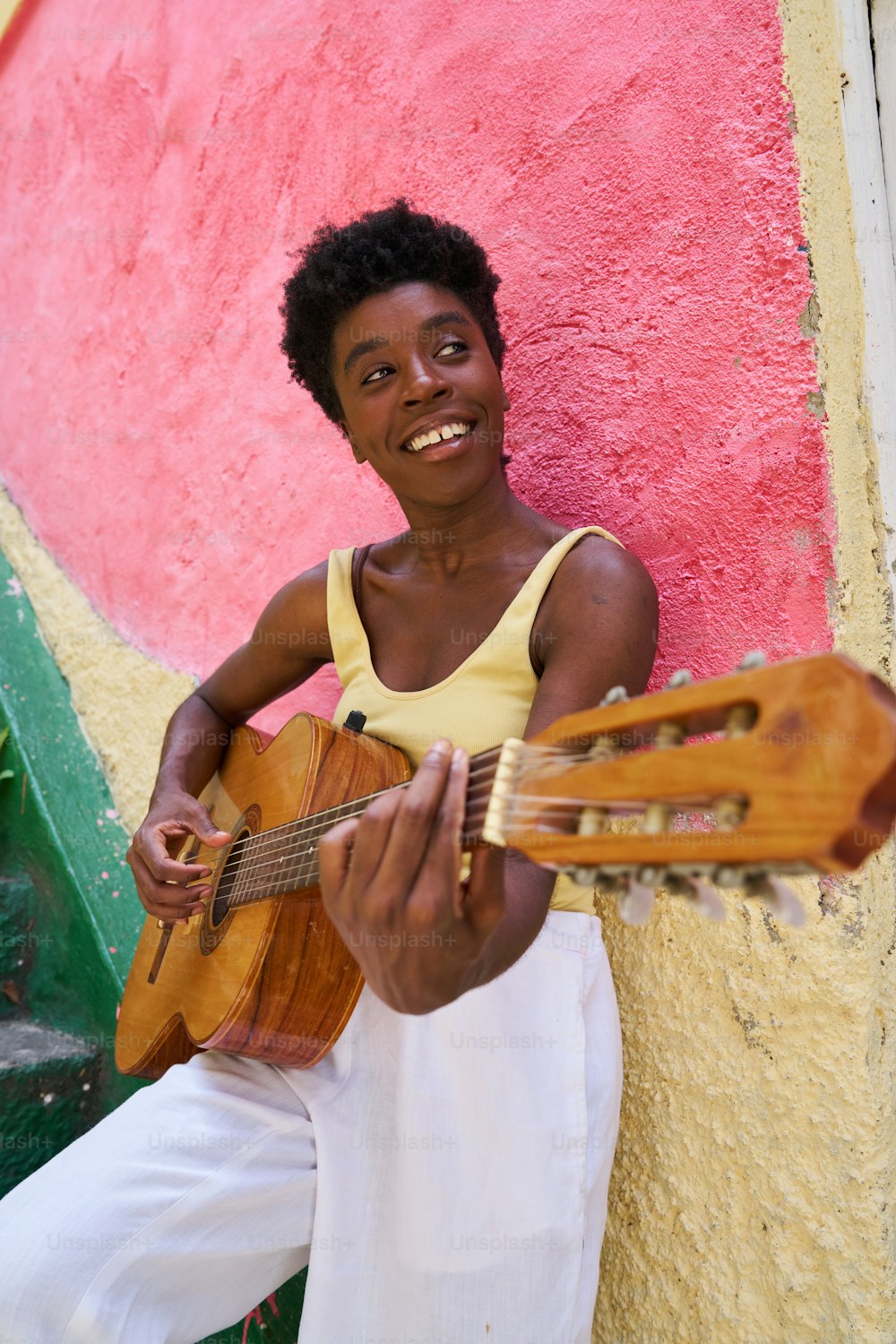 une femme tenant une guitare devant un mur rose et jaune