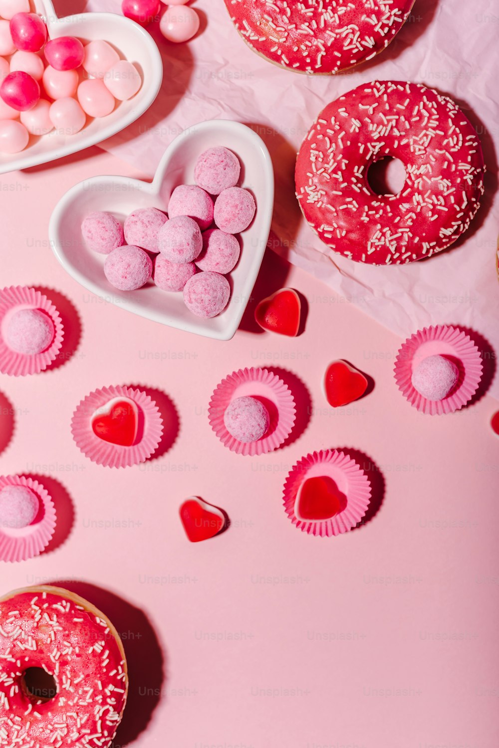 a pink table topped with donuts and heart shaped candies
