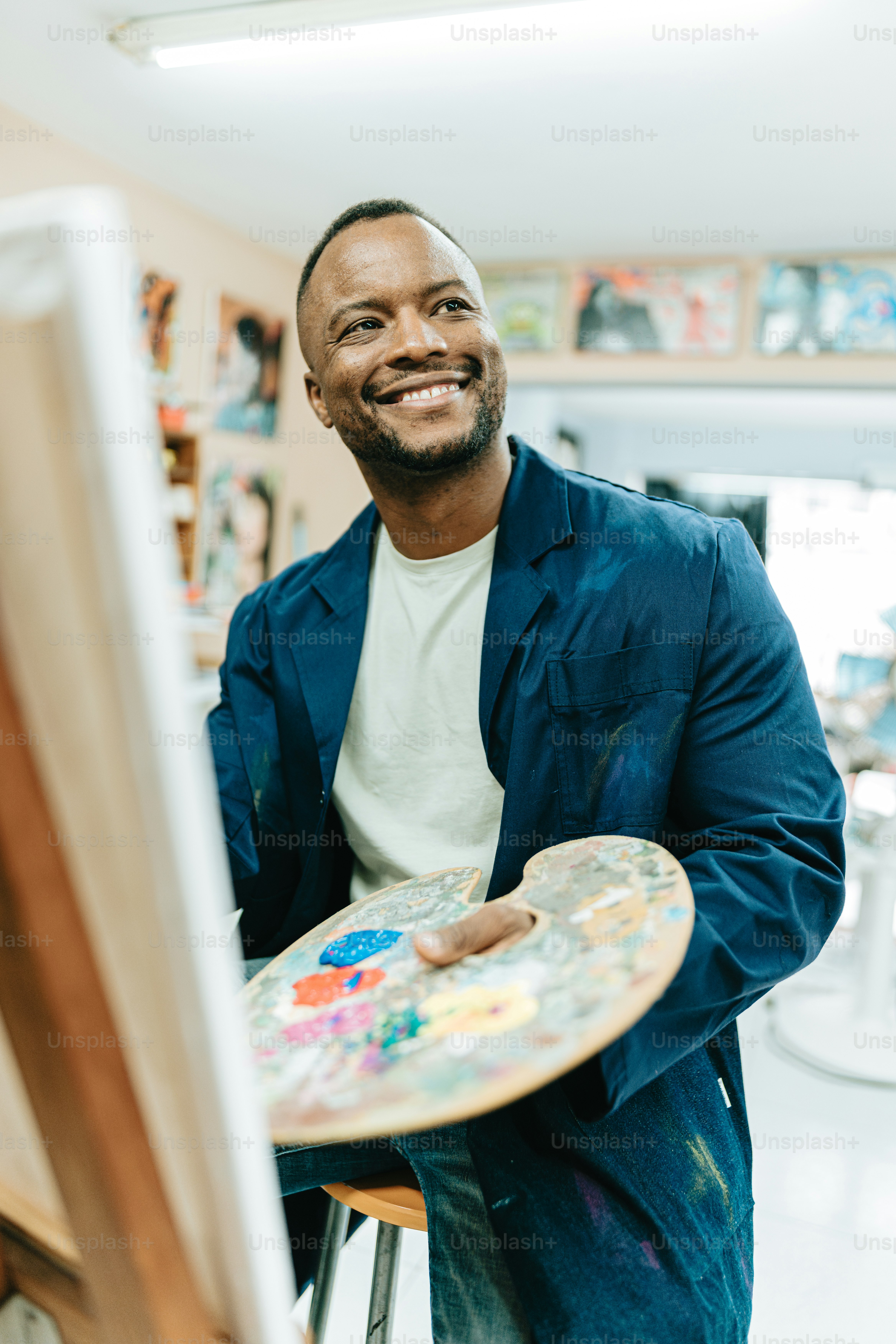 a man sitting in front of a easel holding a paintbrush