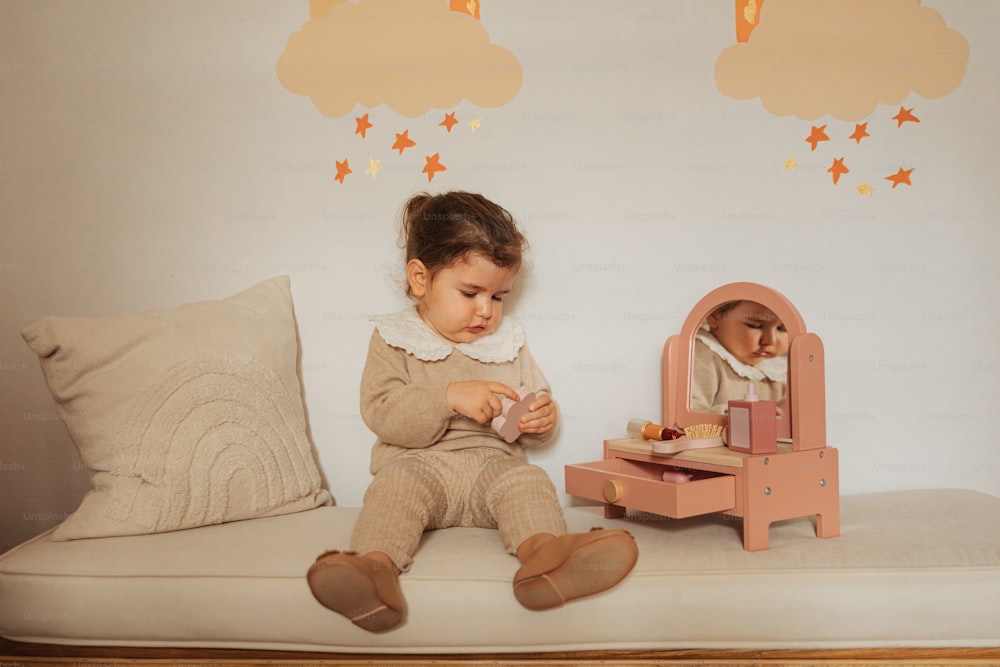 ein kleines Mädchen sitzt auf einem Bett und spielt mit einer Puppe