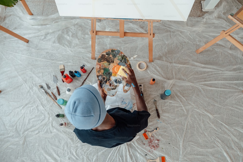 une personne assise sur le sol avec une palette et de la peinture