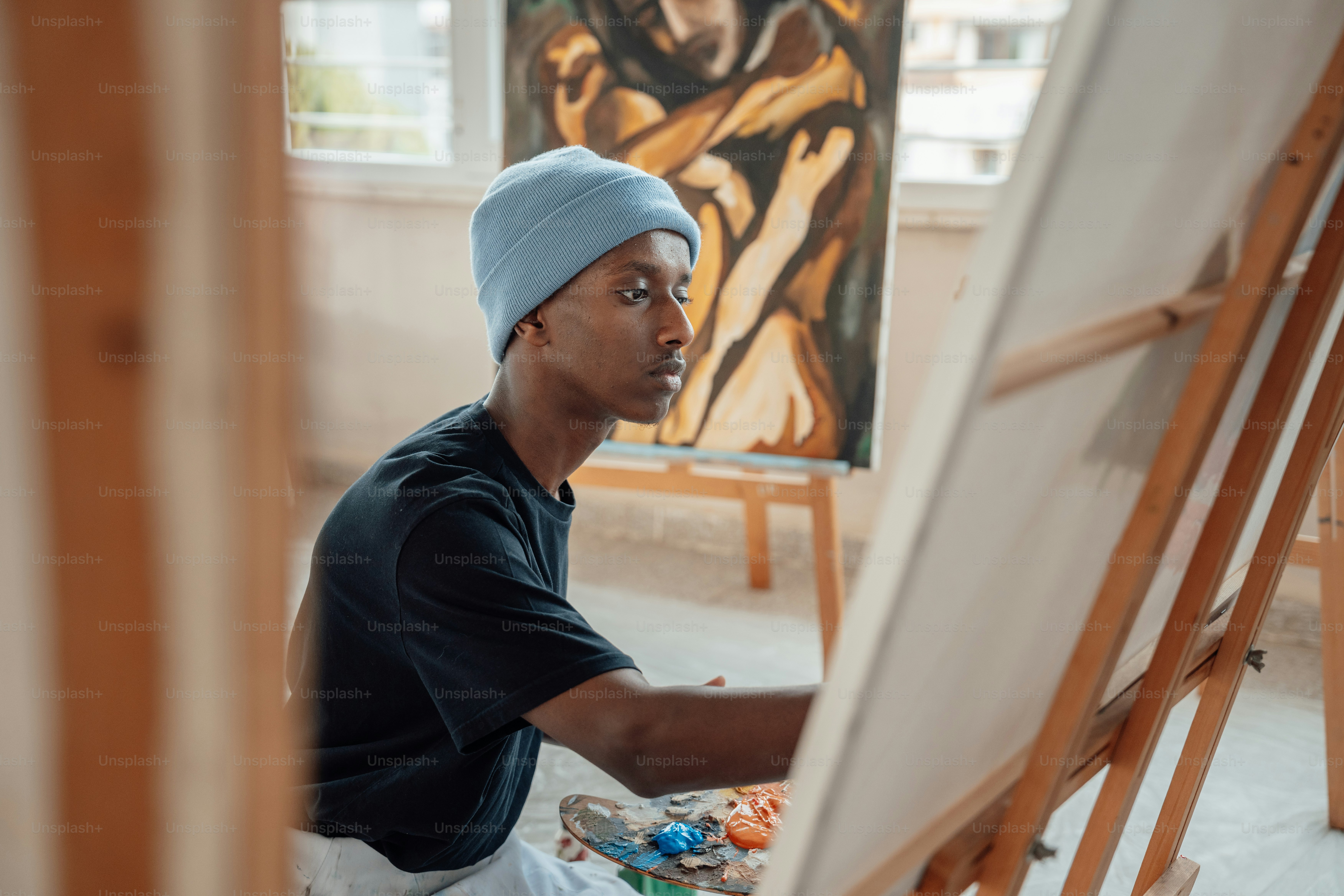 A man sitting in front of a painting on a easel photo – Artist Image on ...