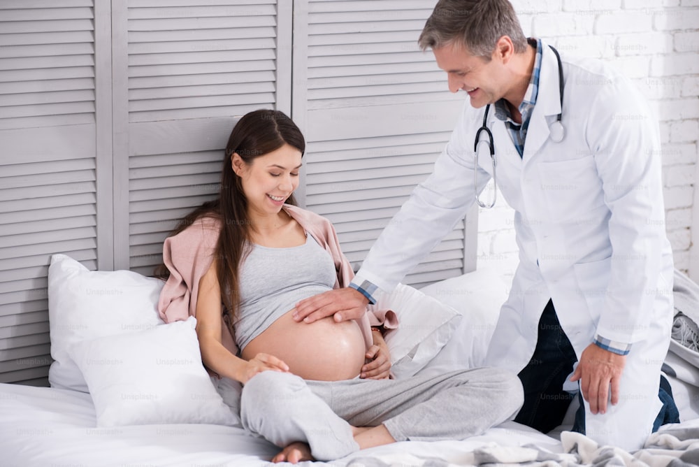 Keep calm. Happy woman expressing positivity while hearing beats of her baby and looking at her bump