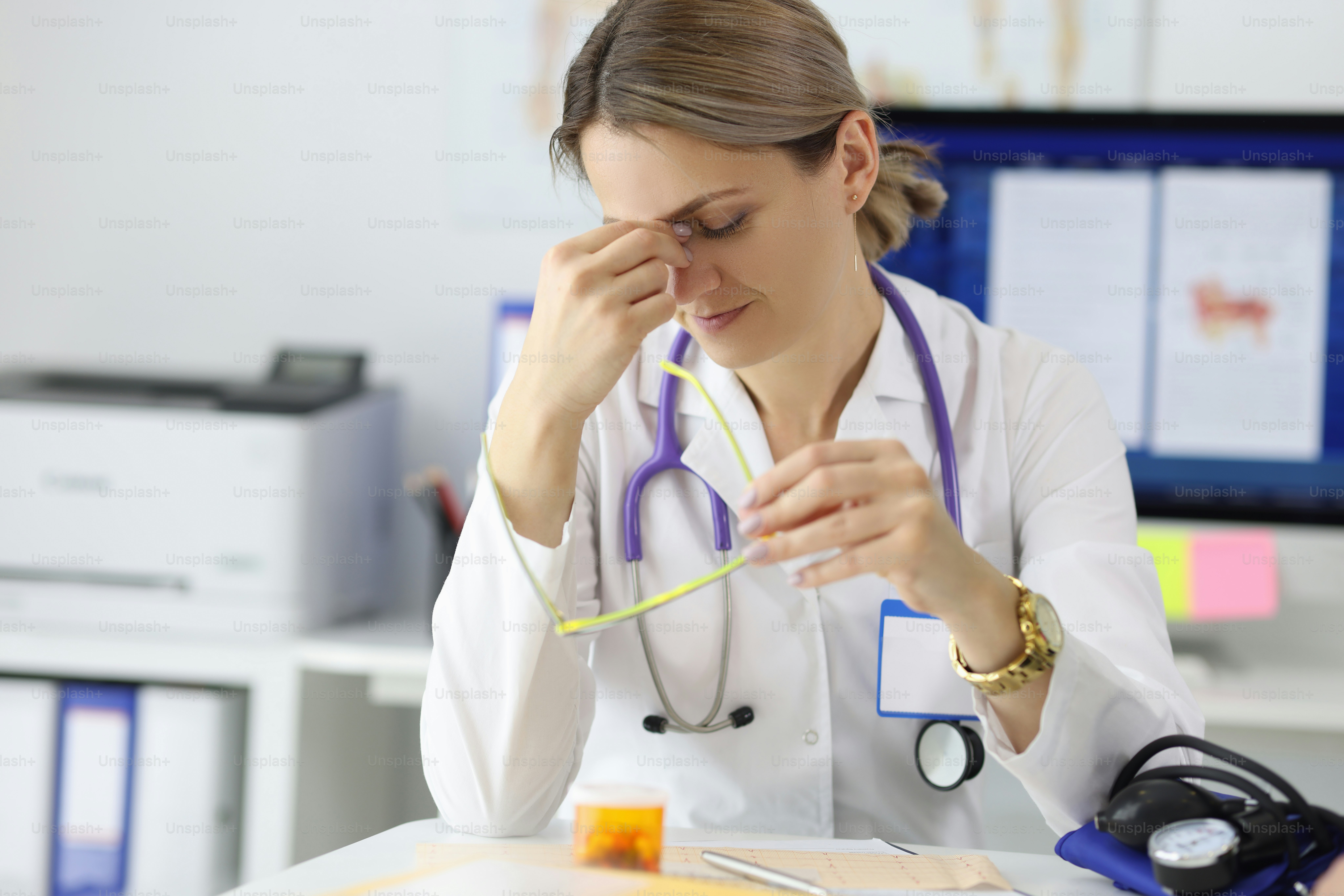 Tired doctor siting at table in his office and looks after his eyes. Increased workload on medical staff recycling concept