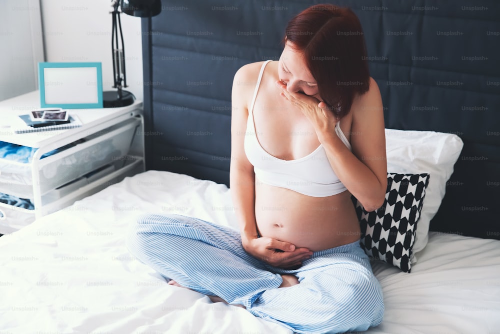 Problems or symptoms of poor health during pregnancy. Pregnant woman suffering with nausea at home interiors. Pregnancy, parenthood, preparation and expectation concept.