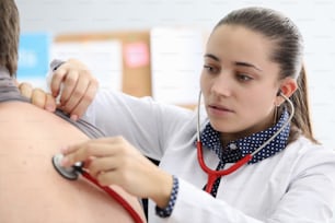 Young woman doctor listens to lungs of patient with red stethoscope portrait. Respiratory system diseases diagnostics concept.