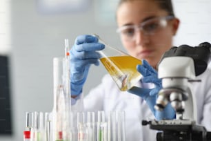 化学実験室で黄色い液体の入ったフラスコを手に持つ女性化学者。石油化学製品のコンセプトの品質管理。