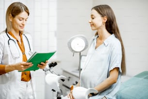 Joven embarazada sentada en la silla ginecológica durante una consulta médica con el ginecólogo. Médico que escribe la historia clínica de un paciente