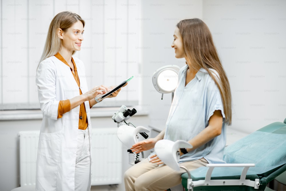 Young pregnant woman sitting on the gynecological chair during a medical consultation with gynecologist. Doctor writing medical history of a patient