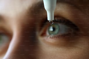視力の問題のクローズアップを解決する彼女の目に液体滴を置く女性