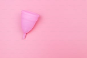 Rosa wiederverwendbare Silikon-Menstruationstasse auf rosa Hintergrund. Draufsicht, Kopierraum. Konzept der Damenhygiene, Gynäkologie und Gesundheit