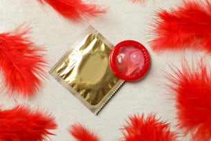 Preservativos y plumas rojas sobre fondo blanco texturizado
