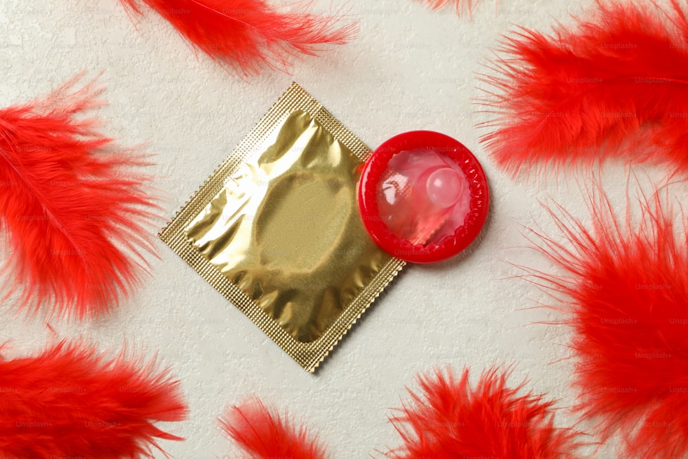 Condoms and red feathers on white textured background