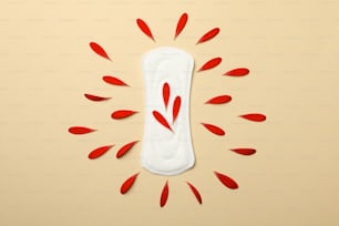 Sanitary pad with gerbera petals on beige background, top view